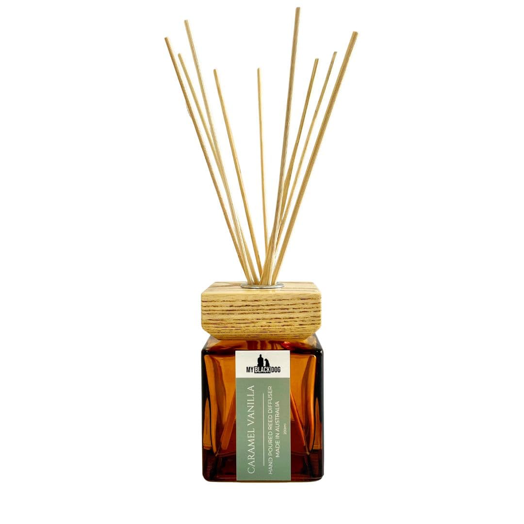 My Black Dog caramel vanilla scented reed diffuser in an amber bottle with wood lid and reed sticks on a white background.