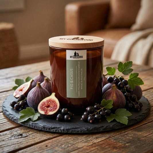 A candle with the label Fig an Cassis sitting on a platter and surrounded by figs and berries