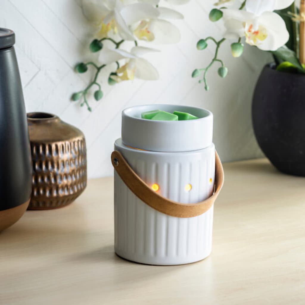 White wax melt warmer with leather handle sitting on a bench top