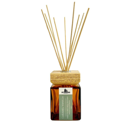 My Black Dog caramel vanilla scented reed diffuser in an amber bottle with wood lid and reed sticks on a white background.