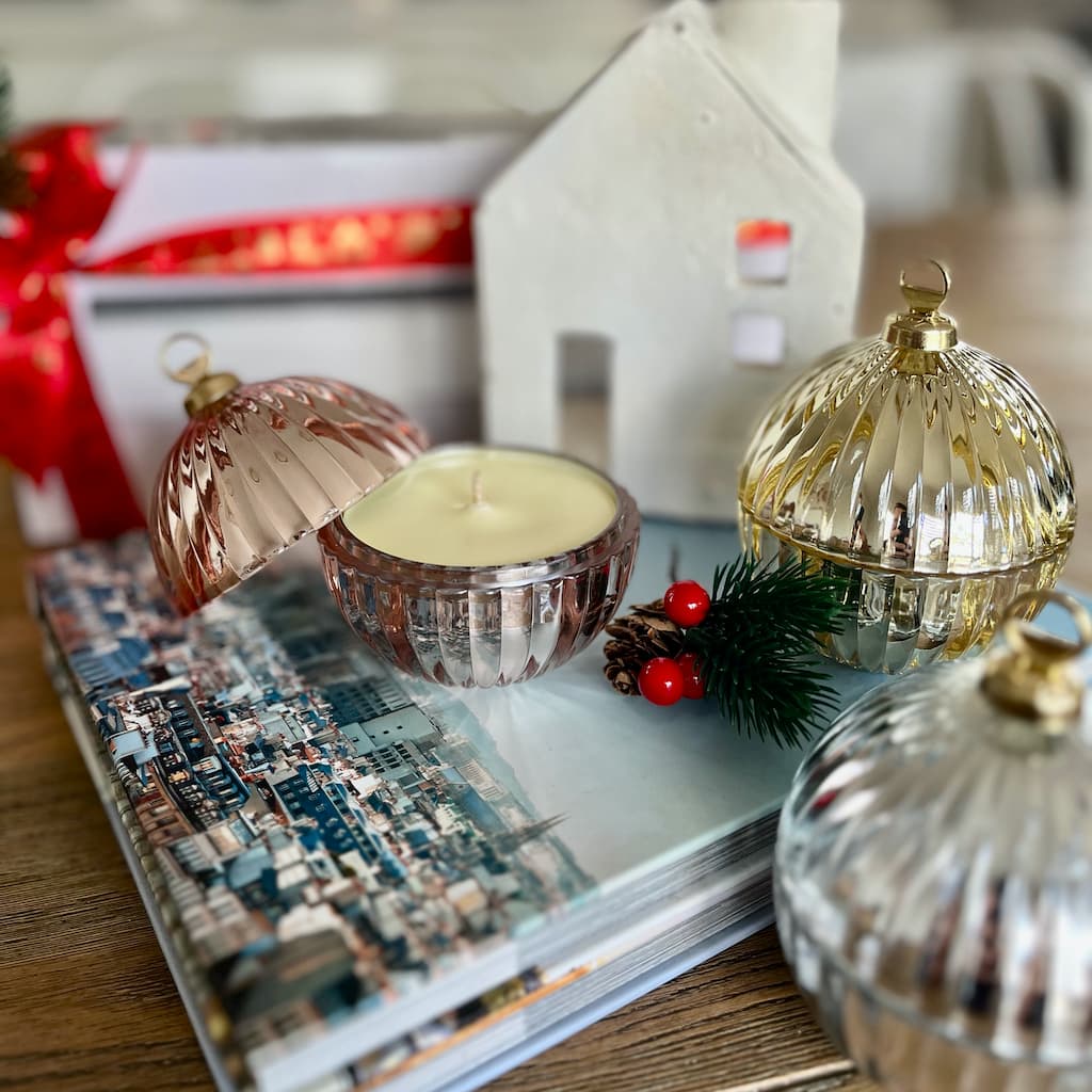 Christmas Bauble Candles sitting on books with a small house and packaging behind it.