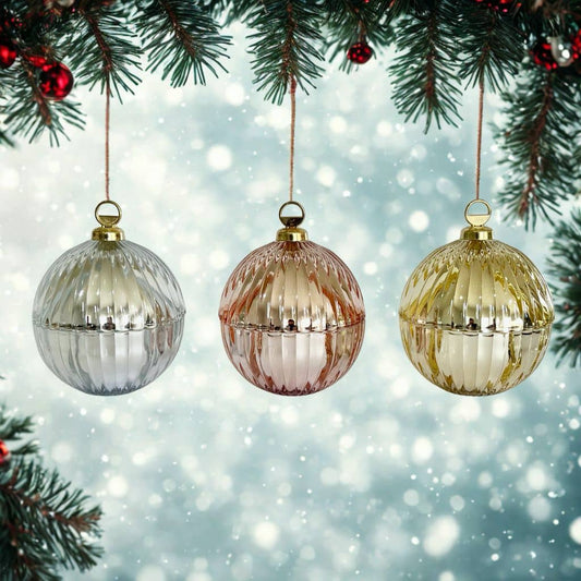 Three ribbed glass ornaments hanging from a Christmas tree with a snowy background.