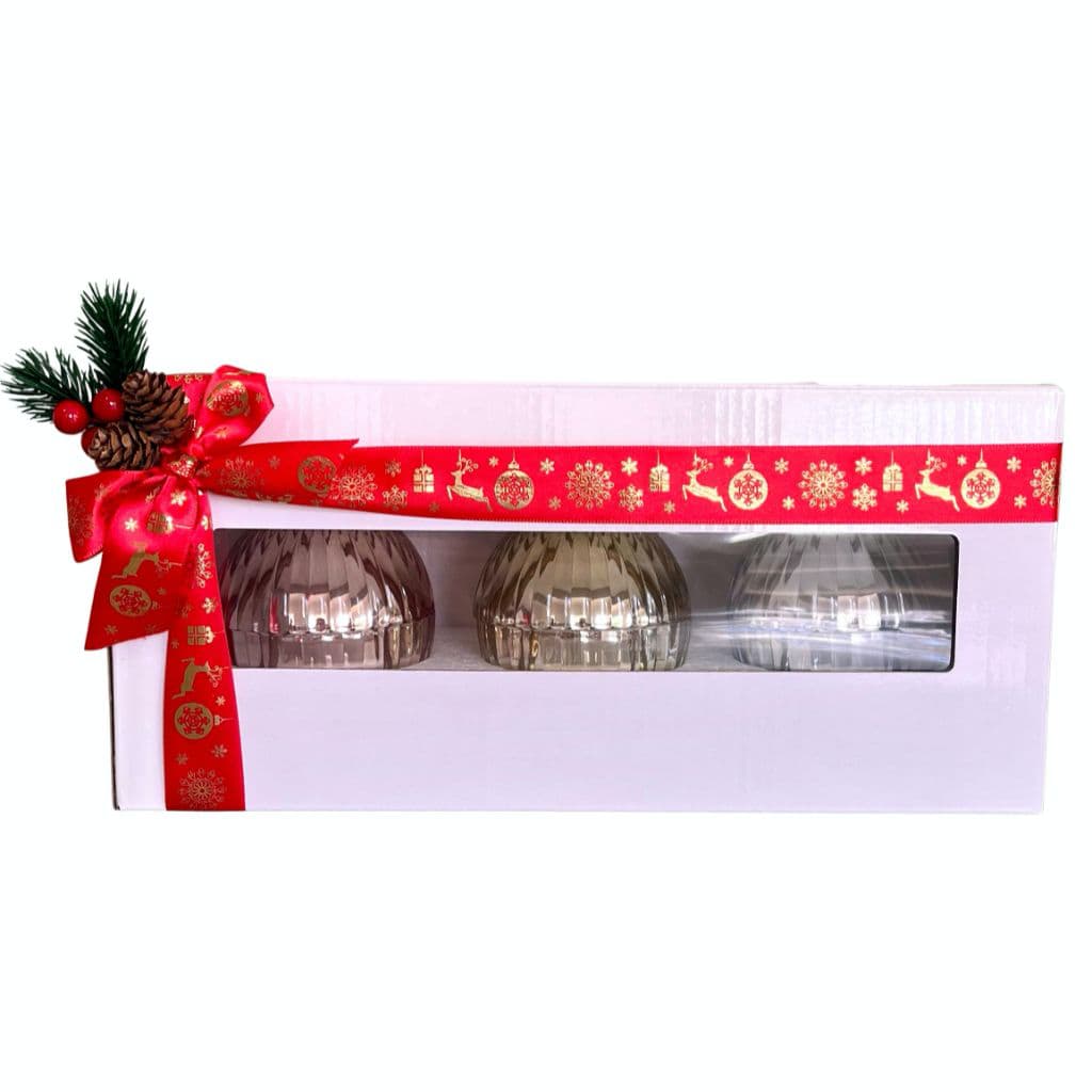Three glass candle ornaments in a decorative box with a red ribbon and Christmas decorations on a white background.