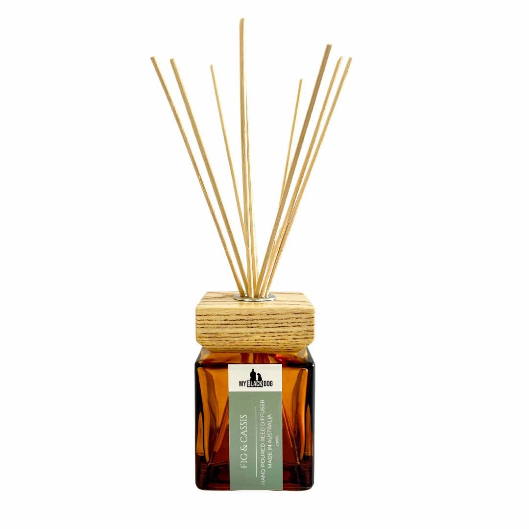 My Black Dog fig and cassis scented reed diffuser in an amber bottle, square wooden lid and reed sticks on a white background.