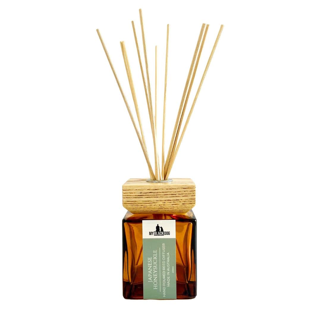 My Black Dog Japanese honeysuckle scented reed diffuser in a square amber bottle with square wooden lid and red sticks on a white background.