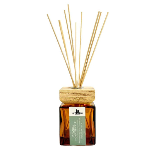 My Black Dog Japanese honeysuckle scented reed diffuser in a square amber bottle with square wooden lid and red sticks on a white background.