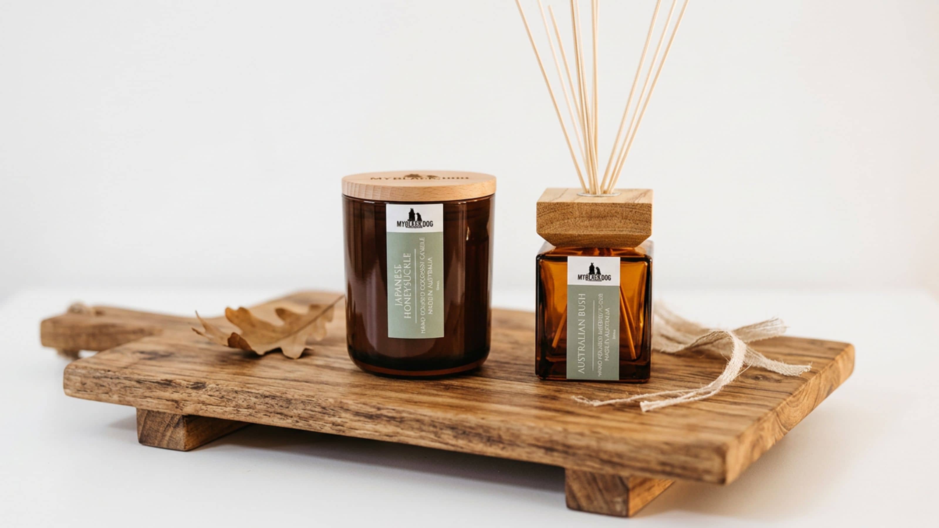 Candle and reed diffuser sitting on a wooden board with a white background