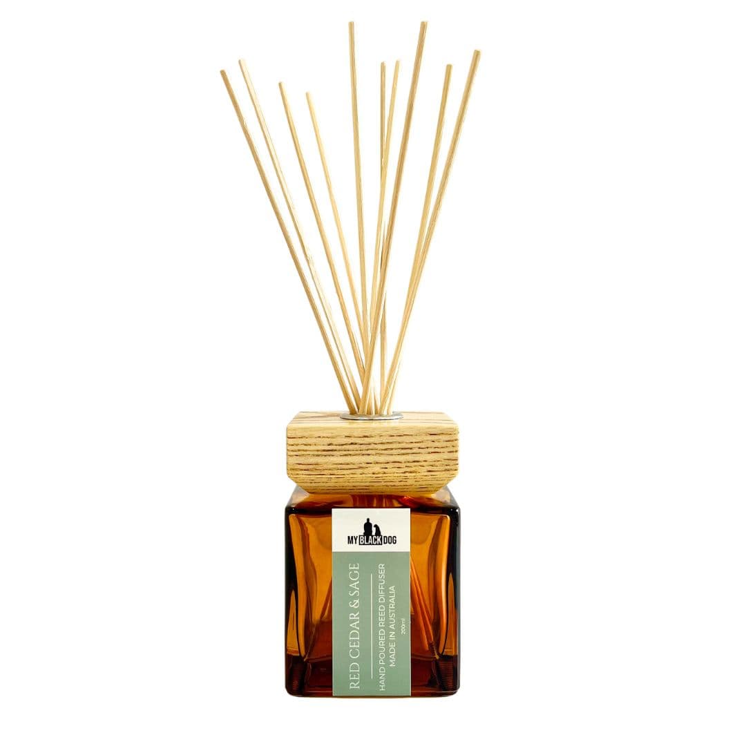 My Black Dog red cedar and sage reed diffuser in an amber bottle, with a wooden lid on a white background