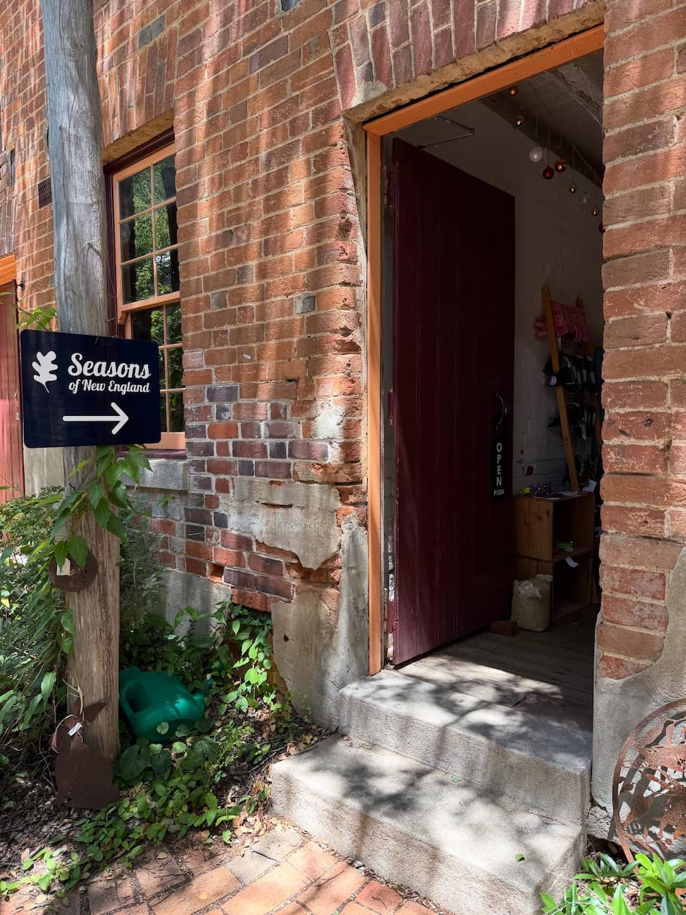 Brick building with an open door, showing a garden area with a 'Seasons of New England' sign.