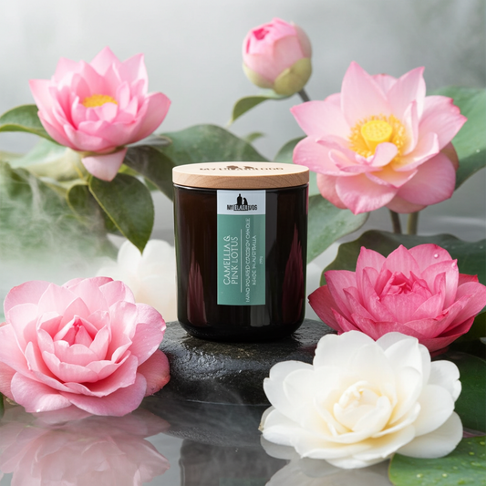 A camellia and pink lotus scented candle sitting on a stone with flowers around it